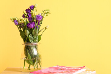 Vase with eustoma flowers and magazine on table near yellow wall
