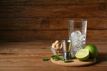 Glass with ice, measure cup and ingredients for preparing mojito on wooden background