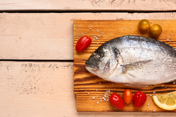 Board of raw dorado fish with tomatoes on light wooden background