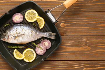 Grill pan of raw dorado fish with lemon and onion on wooden background