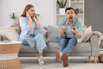 Young couple suffering from loud husband watching TV at home