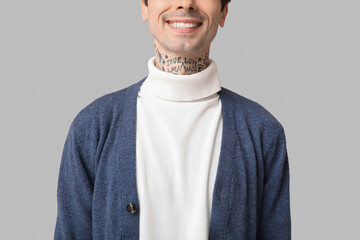 Happy handsome young tattooed man on grey background, closeup