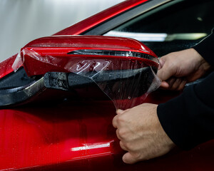 The master applies vinyl film to the side view mirror of a car. 