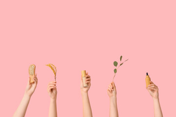 Female hands with hair comb, makeup foundation, mimosa flowers, bottle of serum and branch on pink background