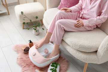 Woman using massage foot bath, spa accessories and eucalyptus branches at home