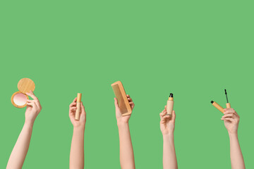 Female hands with highlighter, wooden comb, concealer, foundation and mascara on green background