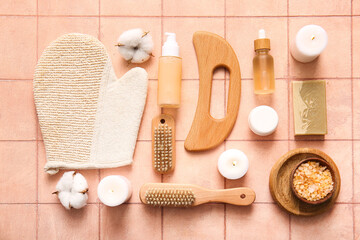 Composition with wooden guasha body massage tool and different bath supplies on pink tile background