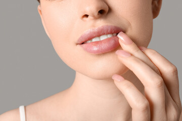 Obraz premium Beautiful young woman applying lip balm on grey background, closeup