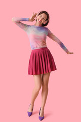Happy young fashionable woman in stylish outfit and headphones on pink background
