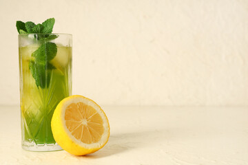 Glass of tasty lemonade with cut lemon and mint on white background