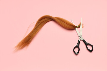 Red hair strand for donation with scissors on pink background