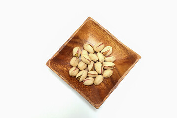 白背景の木製の皿にのせたピスタチオ