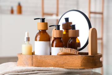 Bottles of cosmetic products and bath supplies in wooden tray on table in bathroom, closeup