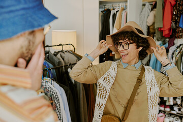 Two people captured in lively interaction in a cozy clothing store, surrounded by vibrant garments and accessories while expressing joy and excitement, one playfully gesturing with a hat