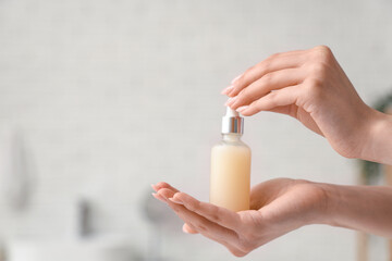 Female hands holding bottle of cosmetic oil in bathroom