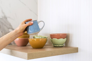 Person placing blue mug on shelf with colorful bowls