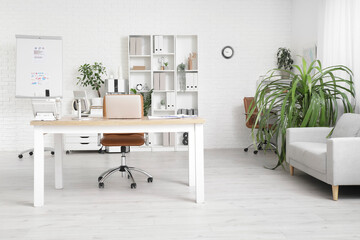 Interior of light office with workplace, armchair, shelving unit and houseplant