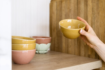 Hand holding a yellow bowl over a kitchen shelf