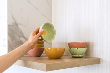 Person arranging colorful bowls on shelf in kitchen