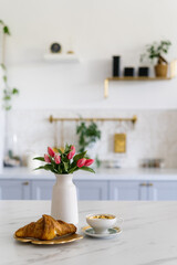 A cozy breakfast setup with flowers, a croissant, and coffee in a modern kitchen