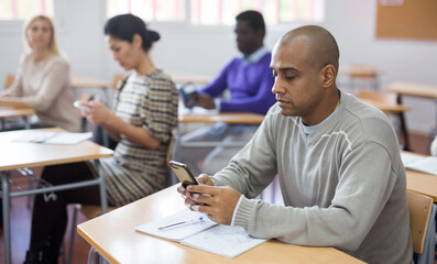 Portrait of focused hispanic man using smartphone to record learning material during lecture in...