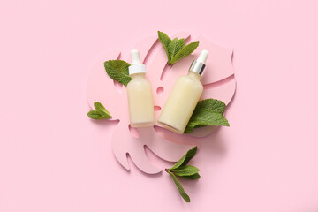 Bottles of essential oil, plaster palm leaf and mint leaves on pink background