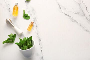 Bottles of essential mint oil, green leaves, mortar and pestle on marble background