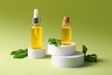Bottles of essential mint oil, plaster stands and green leaves on green background, closeup