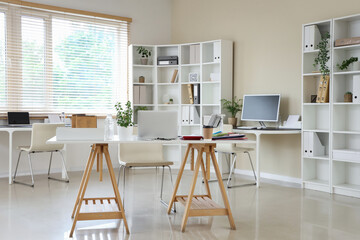 Interior of stylish office with workplaces, laptop and shelving unit