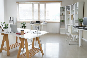 Interior of stylish office with workplaces, laptop and shelving unit