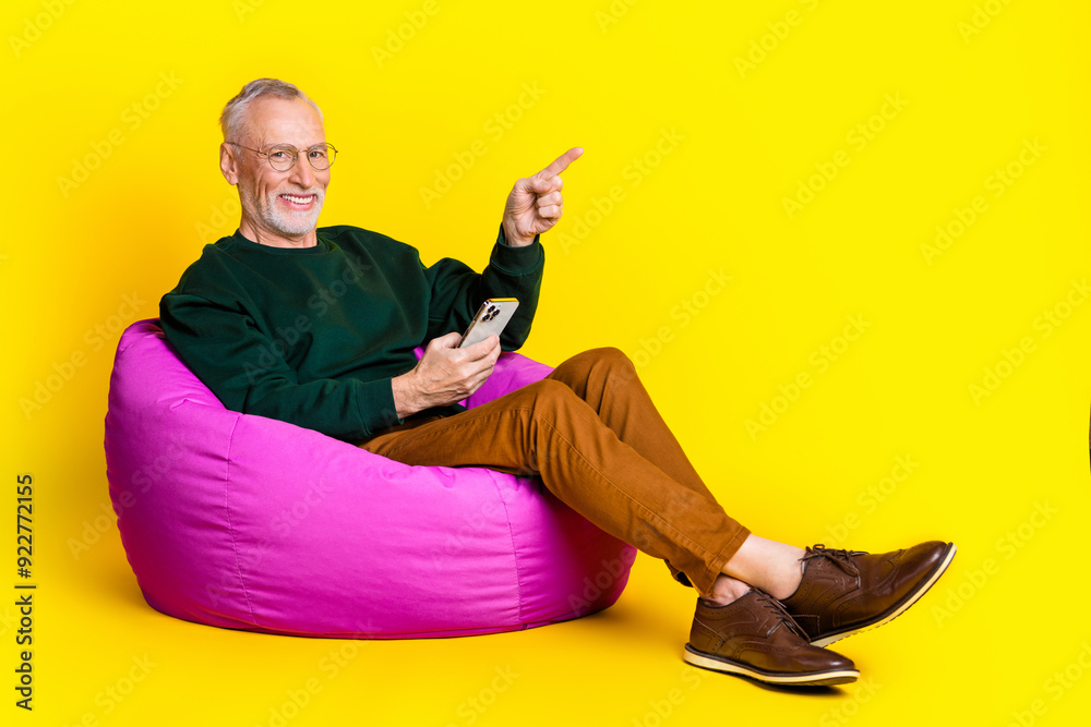 Sticker Full length photo of pensioner man sit beanbag device point empty space dressed stylish green garment isolated on yellow color background