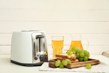 Modern toaster with bread slices and grapes on white wooden background