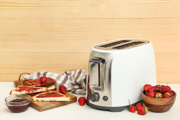 Modern toaster with bread slices, strawberries and jam on white wooden table