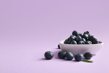 Bowl of fresh ripe blueberry on lilac background, closeup