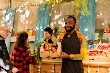 Happy small farm business owner posing at farmers market, wearing apron facing the camera. African american food marketplace vendor selling fresh organic produce and standing at local market.
