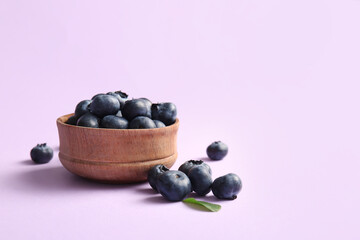 Wooden bowl with fresh ripe blueberry on lilac background, closeup