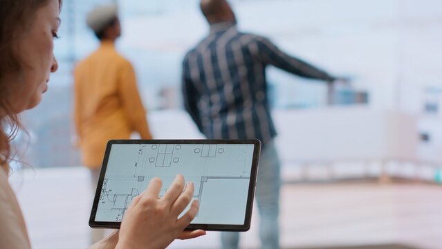 Real estate agent and client evaluating blueprints and discussing the architectural layout of new office space during office tour. Businessman strategizing corporate office relocation deal. Camera B.