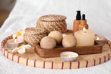 Massage balls with plumeria flowers and burning candles on couch in spa salon, closeup