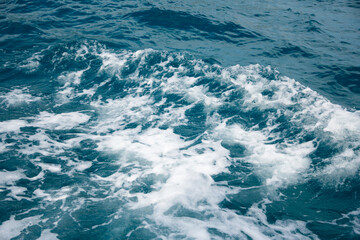 Wave on blue water and white foam on the tops of the waves from under the side of a floating boat, space for text