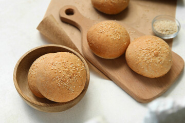 Wooden board and bowl of fresh buns with sesame seeds on white background