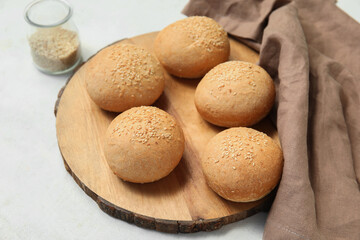 Wooden board of fresh buns with sesame seeds on white background