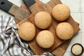 Wooden board of fresh buns with sesame seeds on white tile background