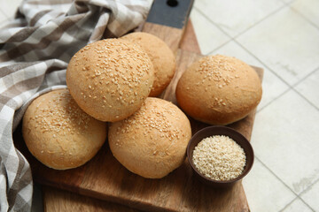 Wooden board of fresh buns with sesame seeds on white tile background