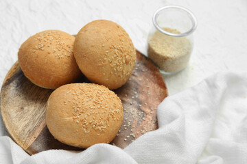 Wooden plate of fresh buns with sesame seeds on white background