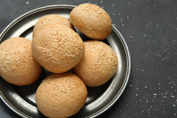 Plate of fresh buns with sesame seeds on black background