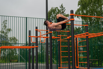 A shirtless man is doing a workout on the horizontal bars outdoors.