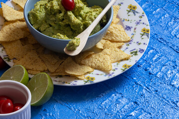 Table consisting of guacamole, nachos, cherry tomatoes and lemon