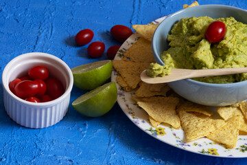 Meal consisting of guacamole, nachos, cherry tomatoes and lemon