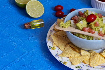 Colorful image of guacamole accompanied by cherry tomatoes and lemon contrasting with a textured blue table