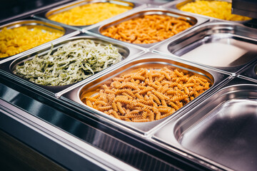 View of a lunch service station with different kinds of pasta in trays.
